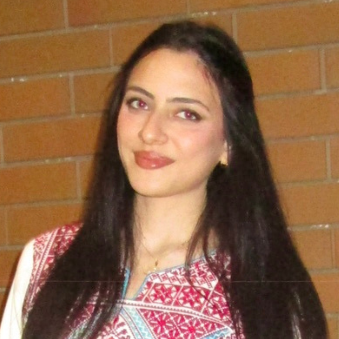 A smiling woman with long dark hair and reddish lipstick wears a white top with red and blue geometric embroidery.