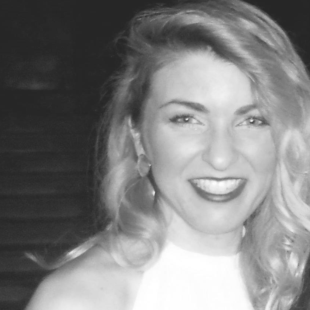 Smiling woman with wavy blonde hair and earrings, smiling broadly at the camera in a black and white headshot.