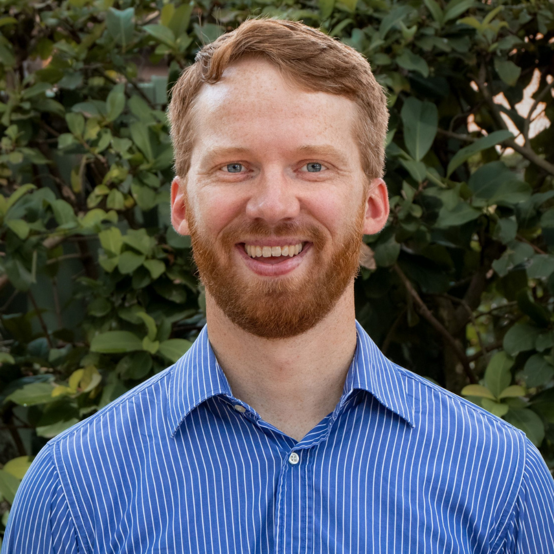 Smiling man with red hair and beard, blue eyes, and freckles, wearing a blue and white striped shirt.