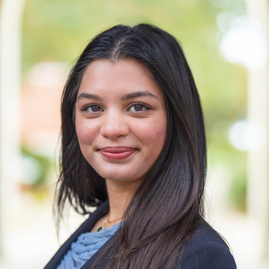 Professional headshot of a young woman with dark hair and a black blazer, smiling.